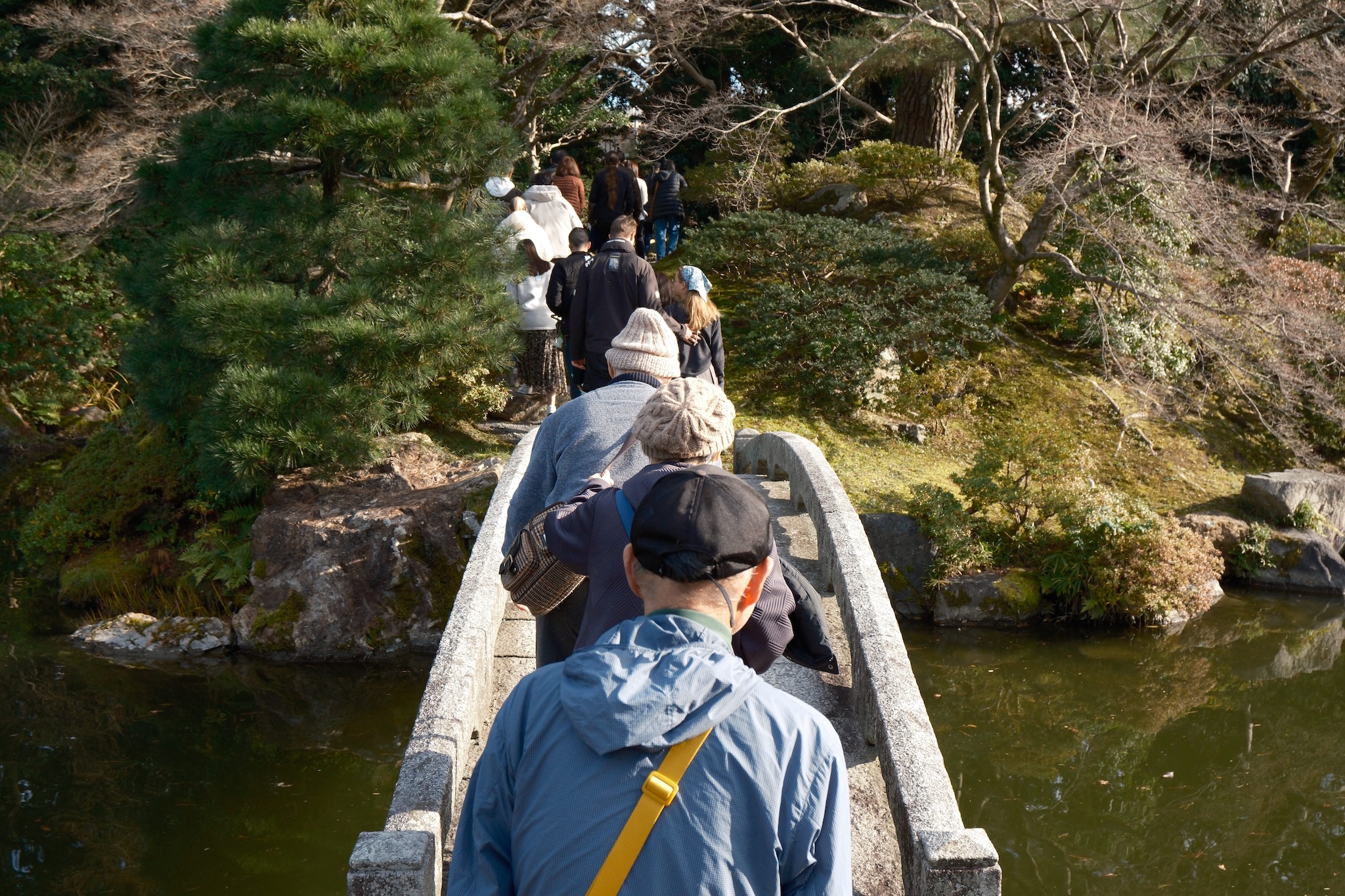 A line of people walking over a wooden bridge taken taken direcrtly from above and behind