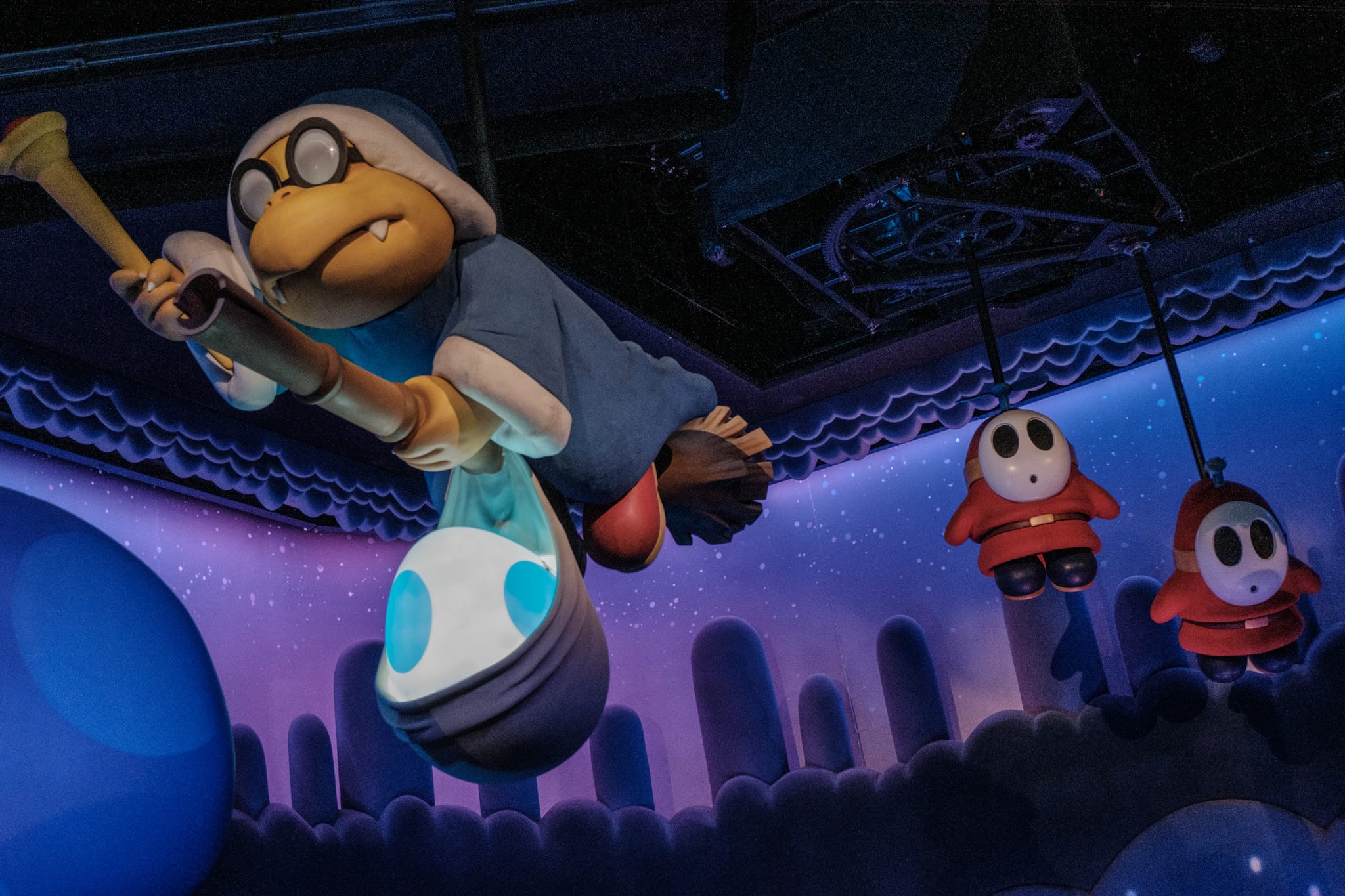 Kamek with a Yoshi egg in a sling with Shy Guys in the background